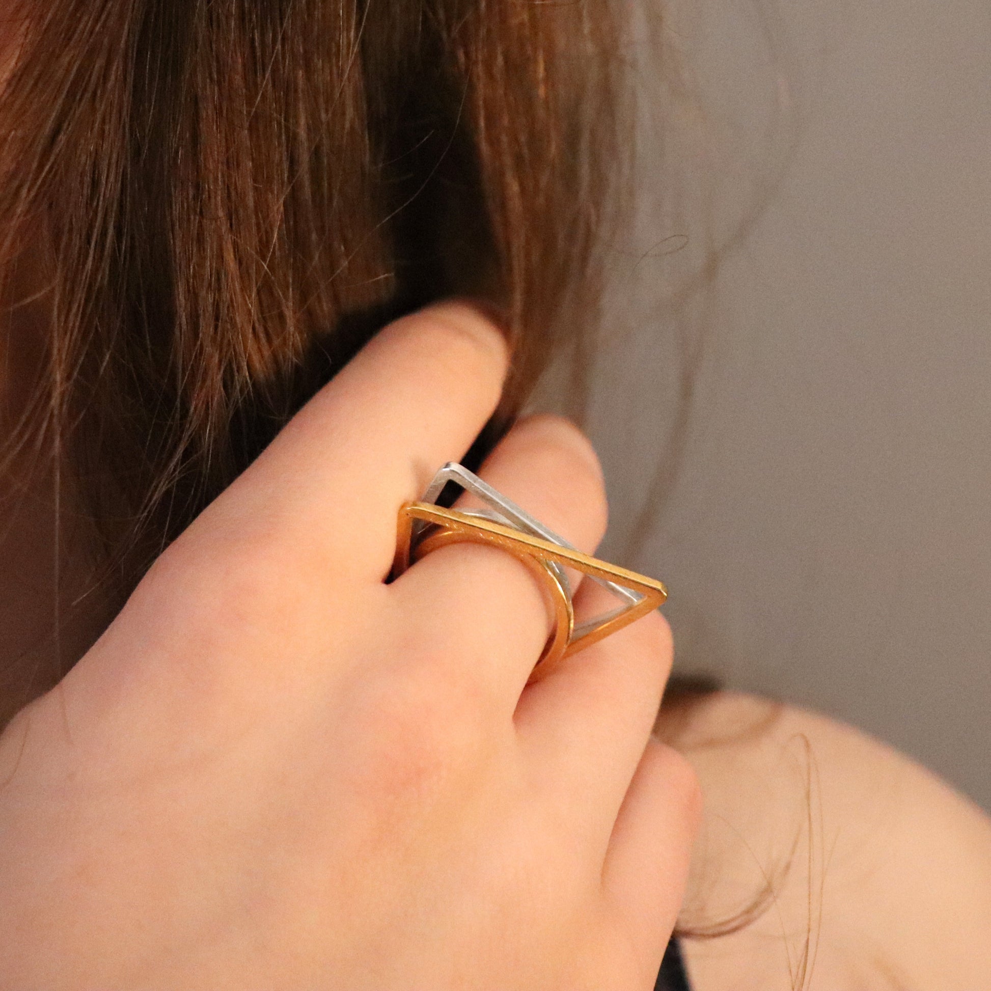Hand wearing a gold and silver ring with a geometric design against a neutral background