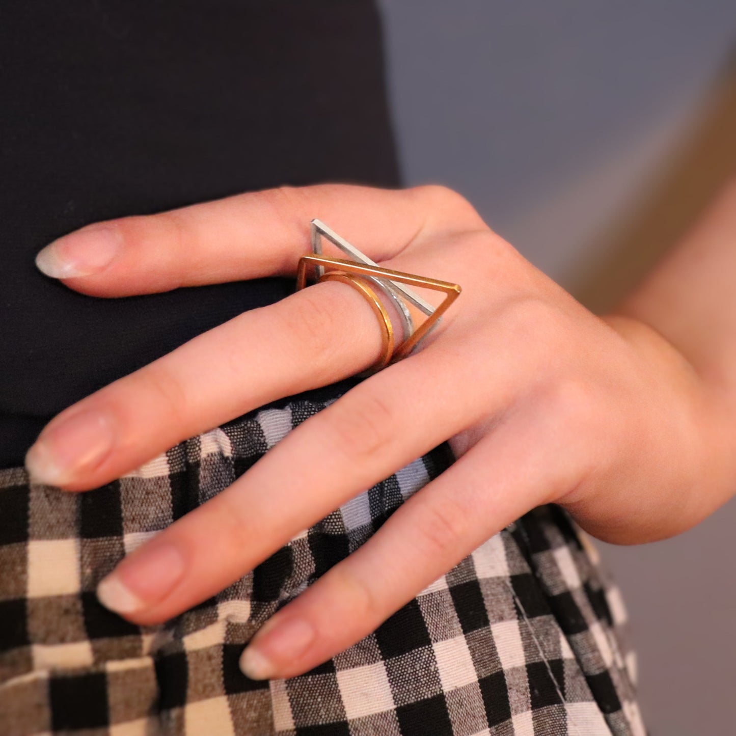 Hand wearing a gold and sivler ring with a geometric design on a blurred background