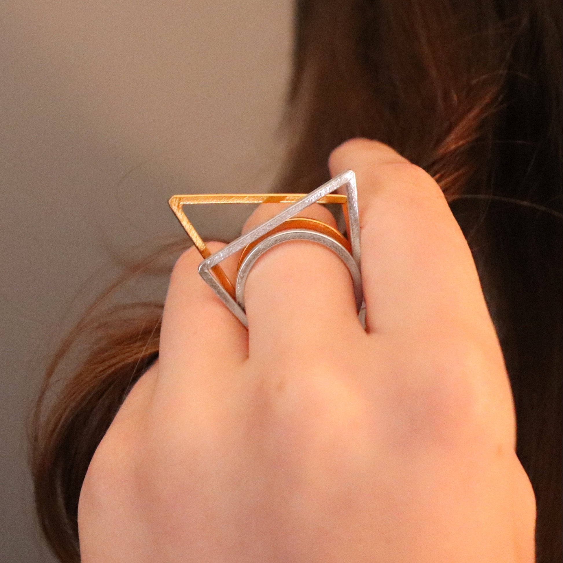 Hand wearing a silver and gold ring with a geometric design on a neutral background