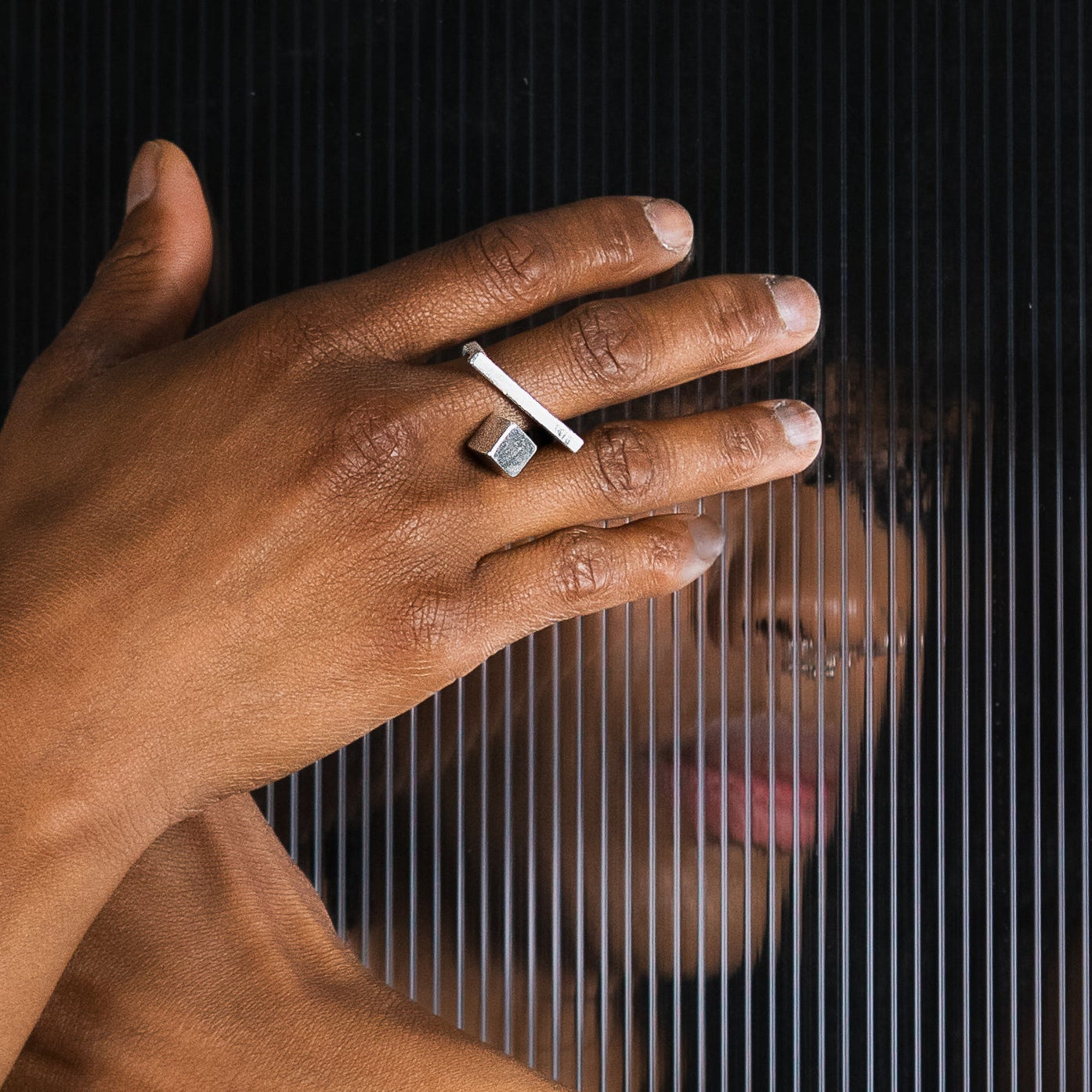 A close-up lifestyle shot of a model showcasing silver architectural ring that has a cube and bar detached from each other, appearing as 2 rings. 