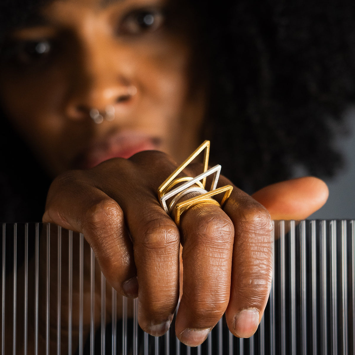 A close-up lifestyle shot of a person wearing geometric gold  and silver stacking rings. 