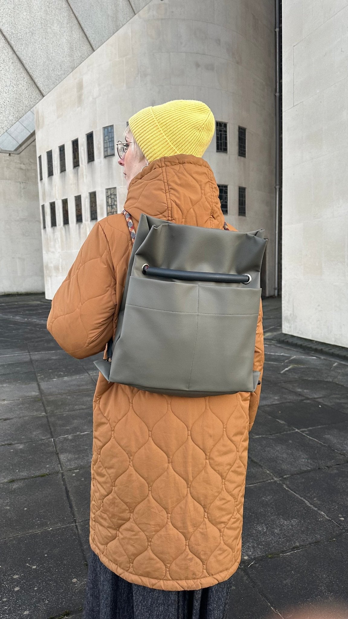 Olive-grey Ditto backpack modelled by blond by modern brutalist architecture