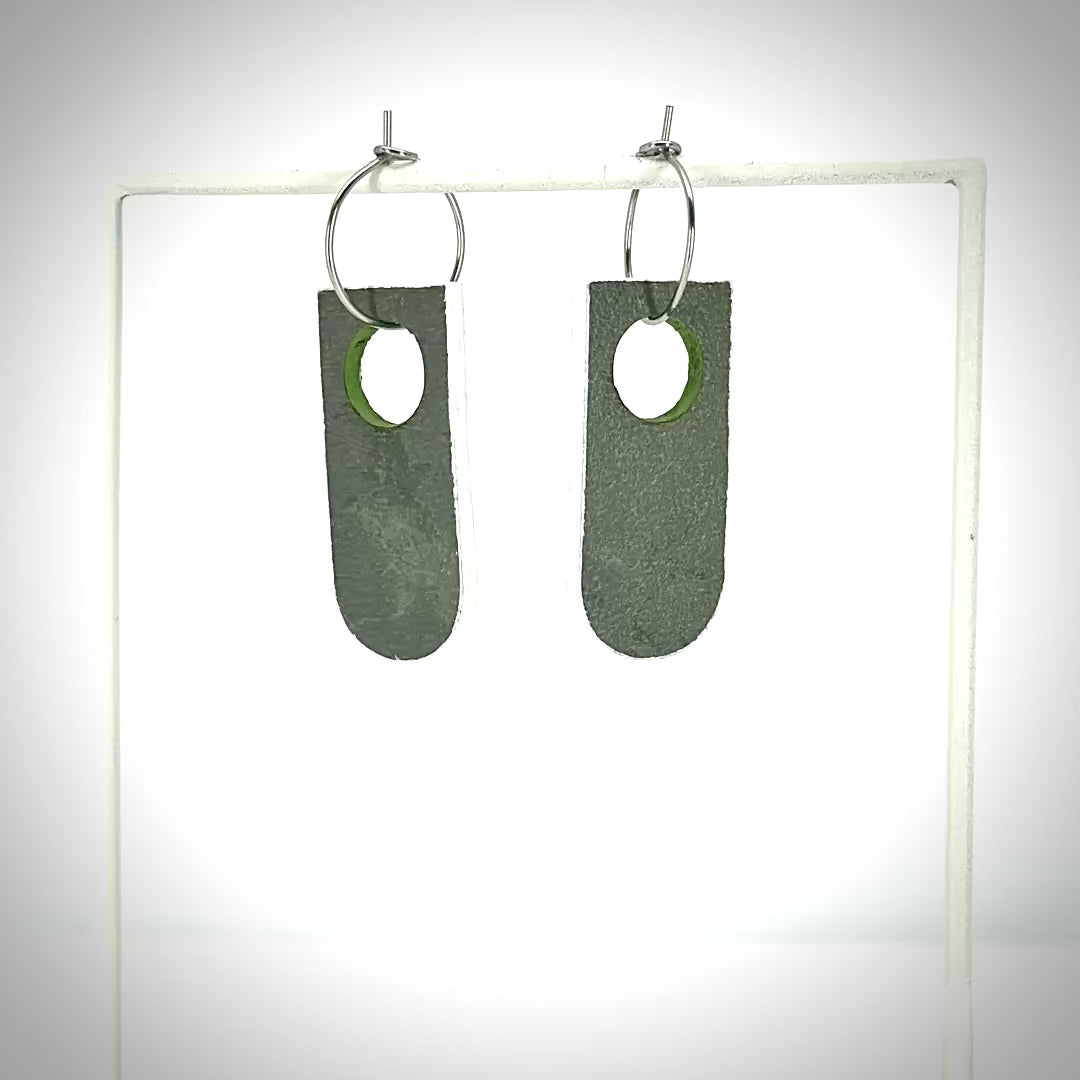 rotating grey and green earrings on an earring stand