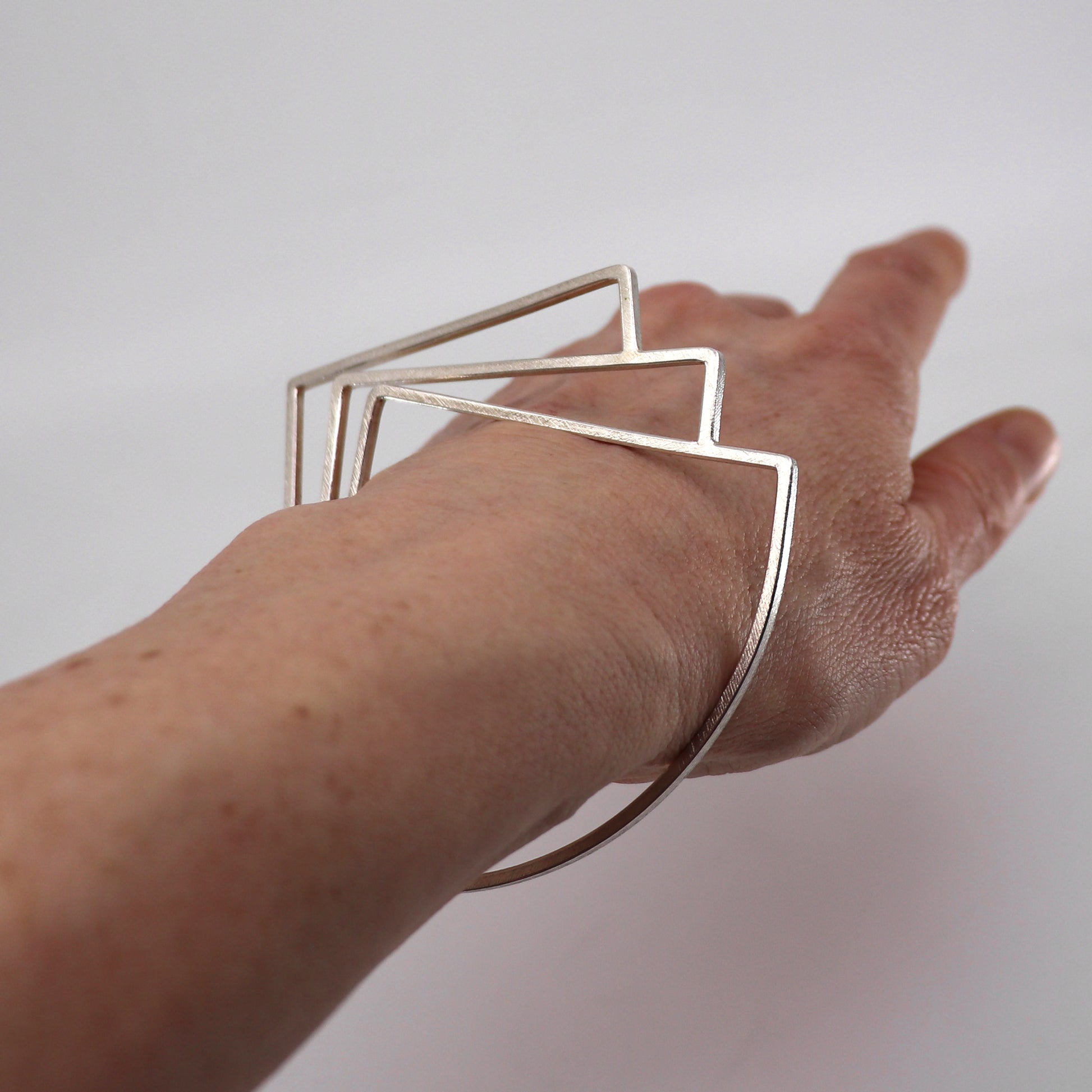 Hand wearing a silver geometric bracelet on a plain background